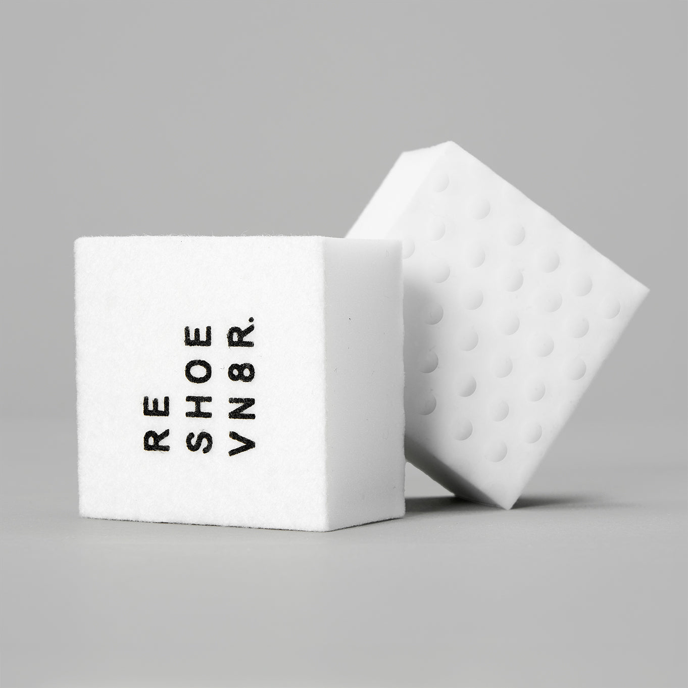 Two white sponges stacked on top of each other on a gray surface. There is text on the sponges that says "RESHOEVN8R". One sponge has soft side and one sponge has bumpy side.