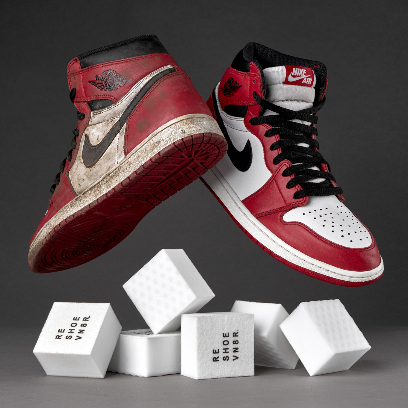 A pair of red, black and white Nike Air Jordan 1 sneakers floating in mid air next to a stack of white shoe cleaning sponges on dark grey background. The text "NIKE AIR" is visible on the side of the sneakers. Cleaning sponges have black text print that reads "RESHOEVN8R". One shoe is visibily dirty, and the other is clean.
