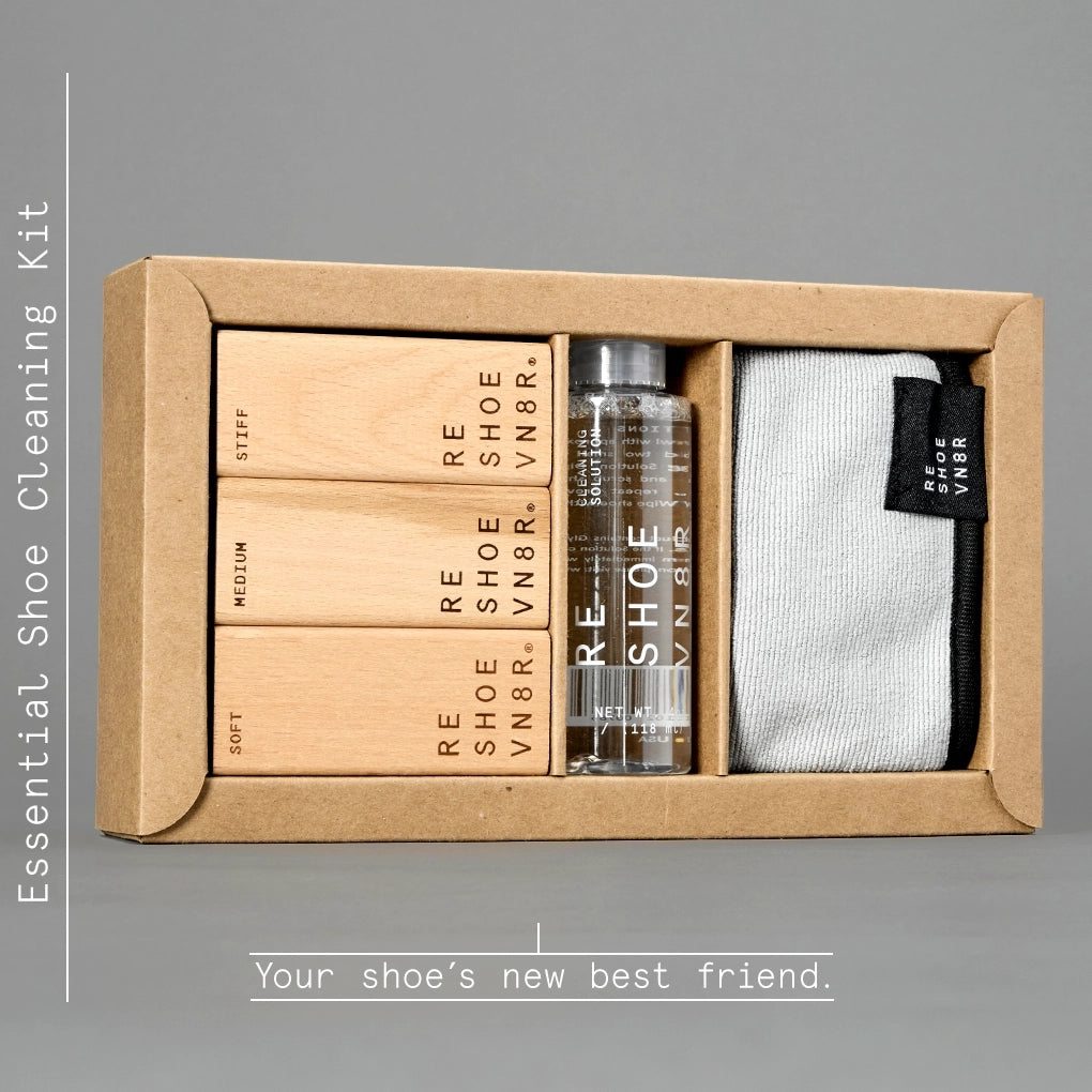 A box of Reshoevn8r Essential Shoe Cleaning Kit resting on a white background. The kit includes a bottle of cleaning solution, three brushes in different softness levels (soft, medium, and stiff), and a microfiber towel. Text on the box indicates the brushes are for use on suede, leather, mesh, canvas, nubuck, plastic and rubber shoes.